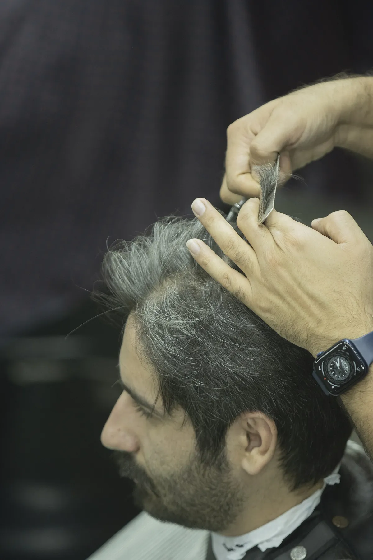 Foto de exemplo: barbeiro acertando com tesoura o cabelo grisalho de um cliente de barba