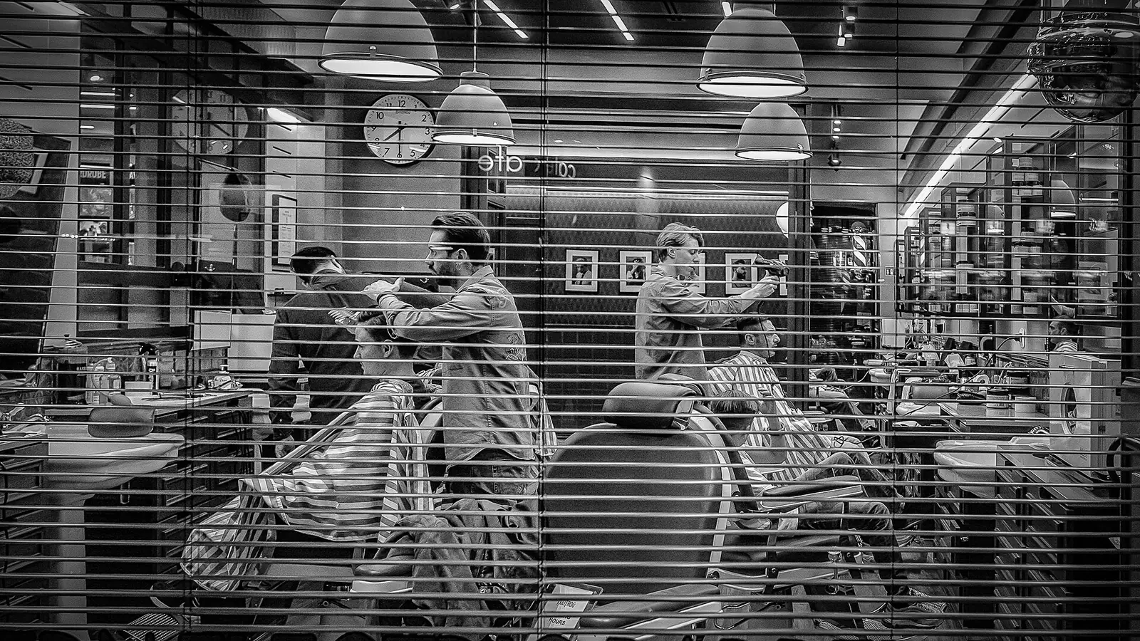 Salão de barbearia com barbeiros atendendo, em preto e branco